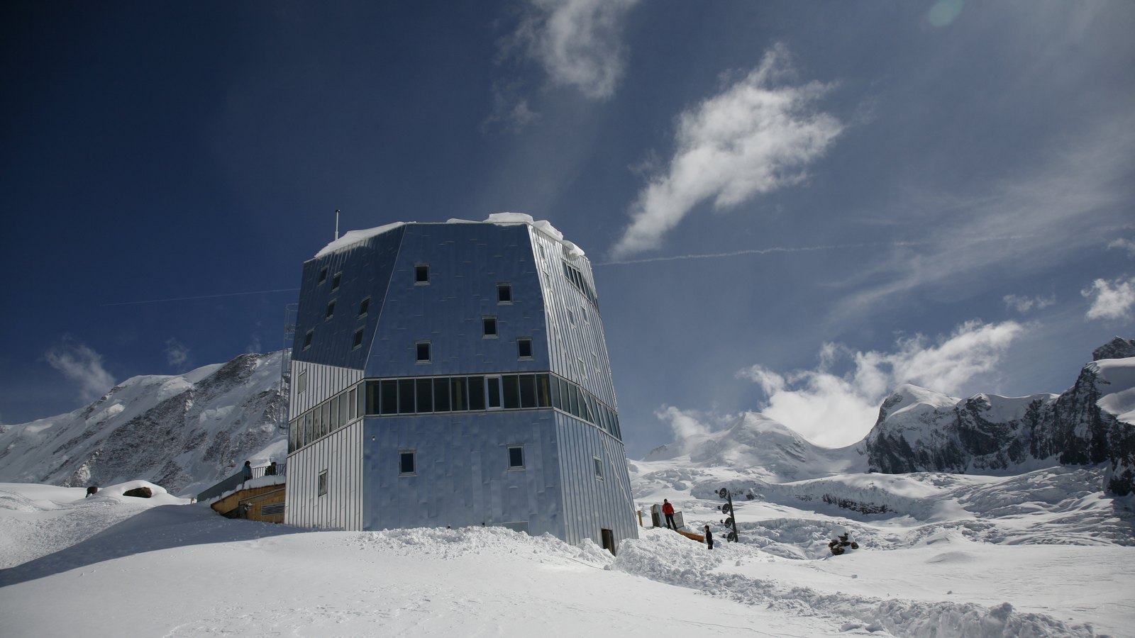 Die mehrflächige, silbern verkleidete Neue Monte Rosa Hütte im Schnee vor Gletscher und Bergen