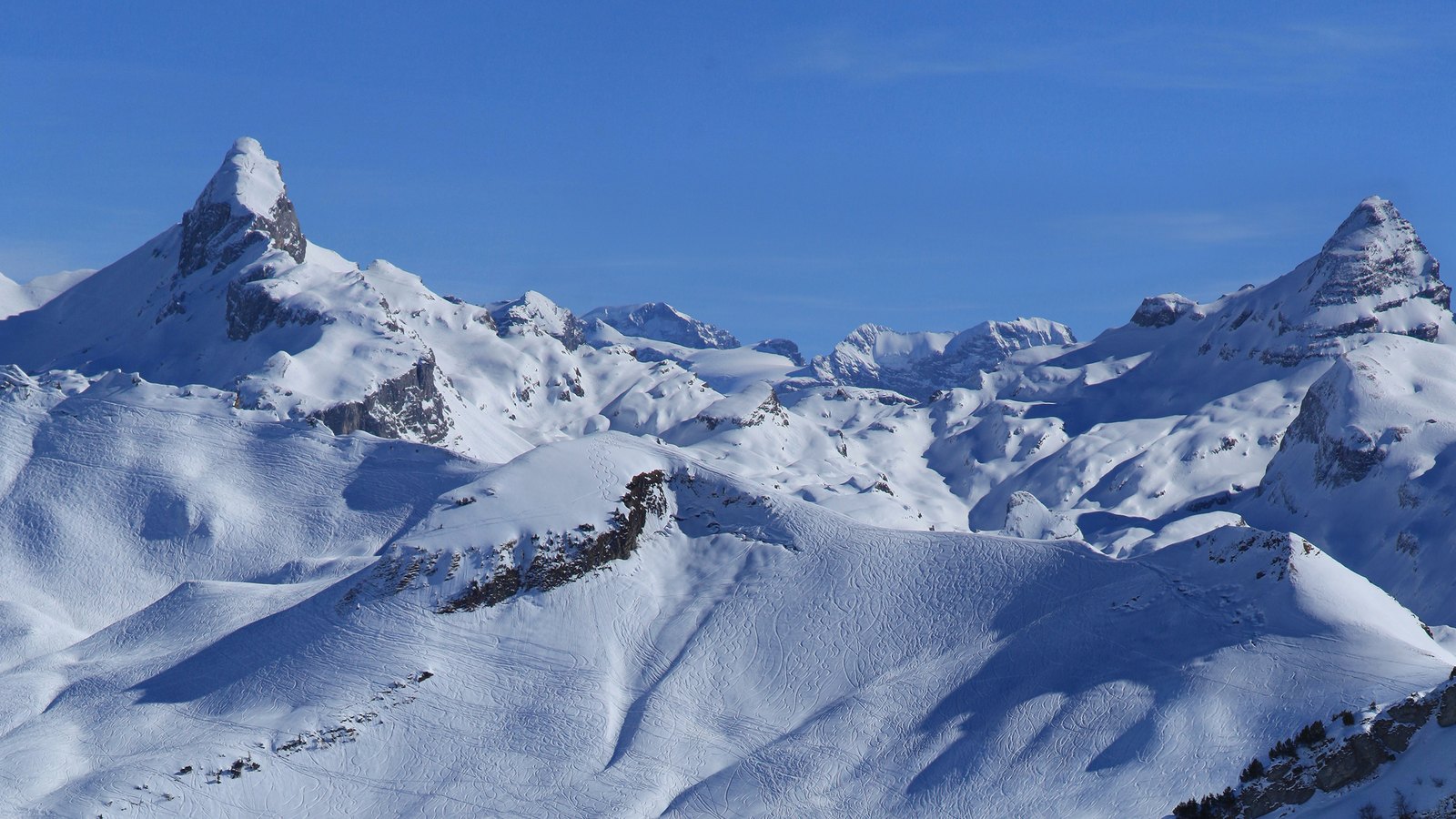 Tief verschneite Berge mit spitzen Felsgipfeln unter blauem Himmel im Winter am Stoos